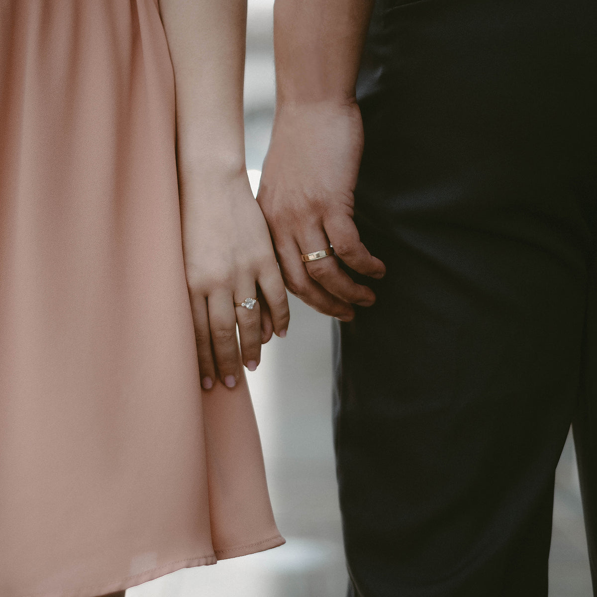 Woman wears petite three-stone ring and man wears yellow gold wedding band