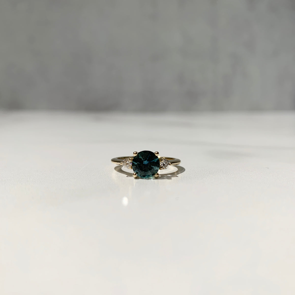 Yellow gold three-stone ring with round teal sapphire center